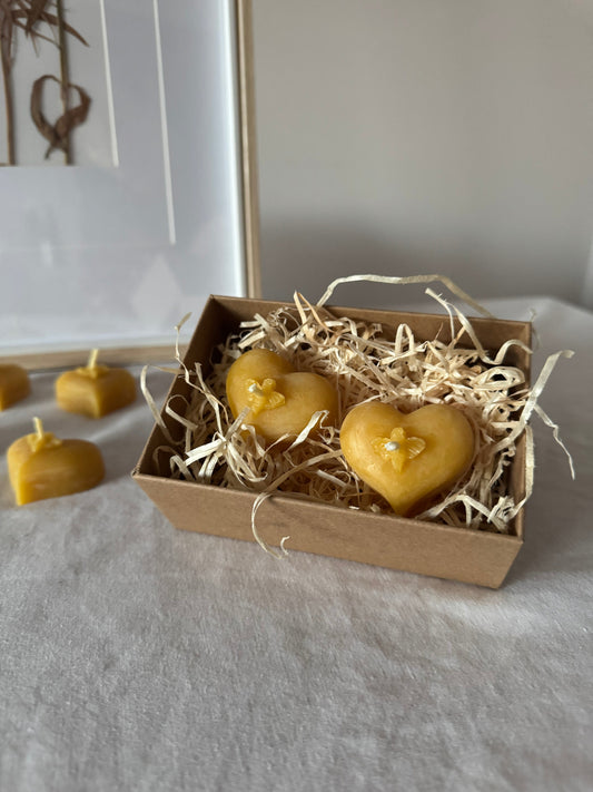 A pair of heart shaped tealights, heart shaped candles, in a box made of kraft packaging which is sustainable packaging, sit on a bed of wood wool, and a cream linen