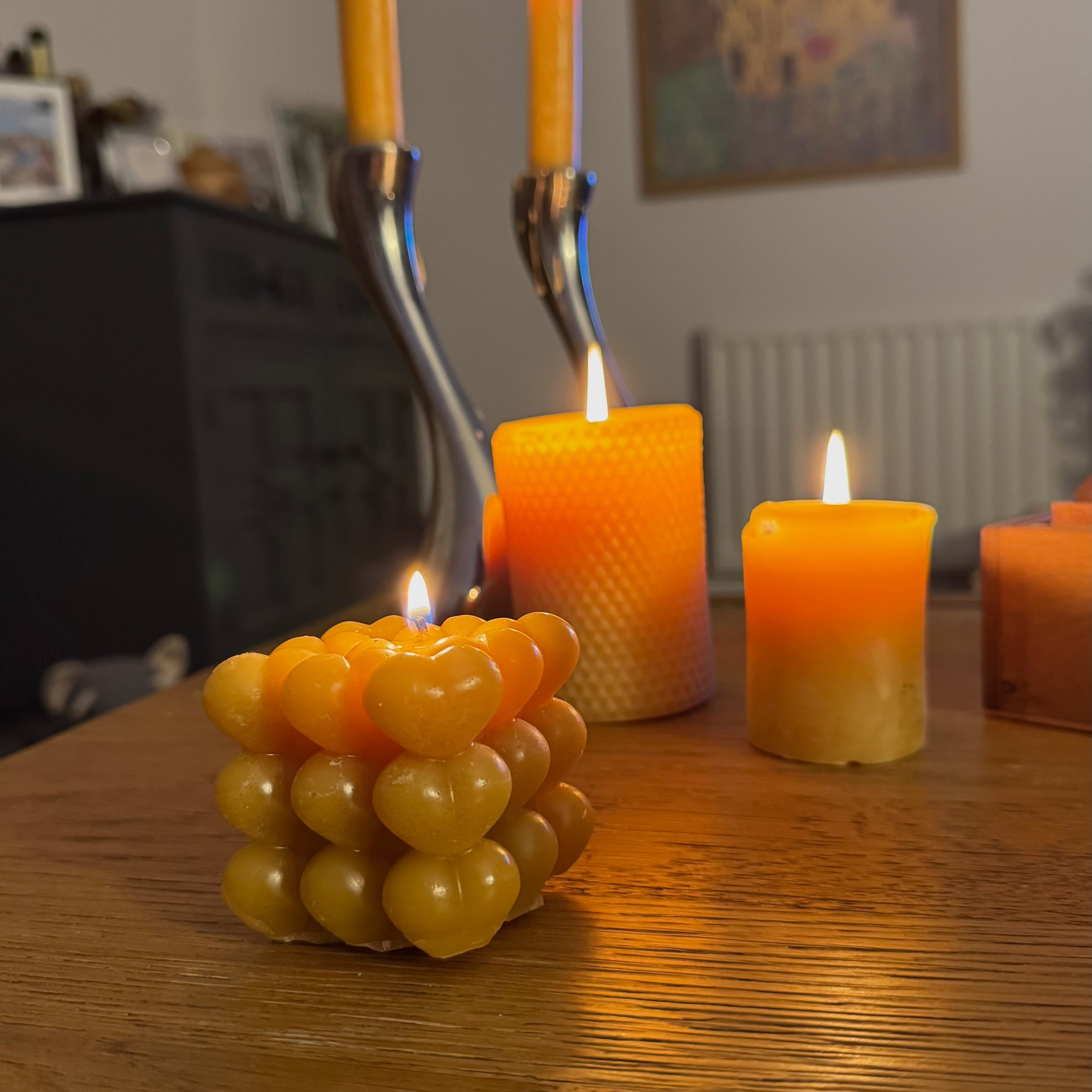 A heart shaped bubble candle, positioned on a soft grey side with beeswax pillar candles, burning in the background creating a homely, natural vision