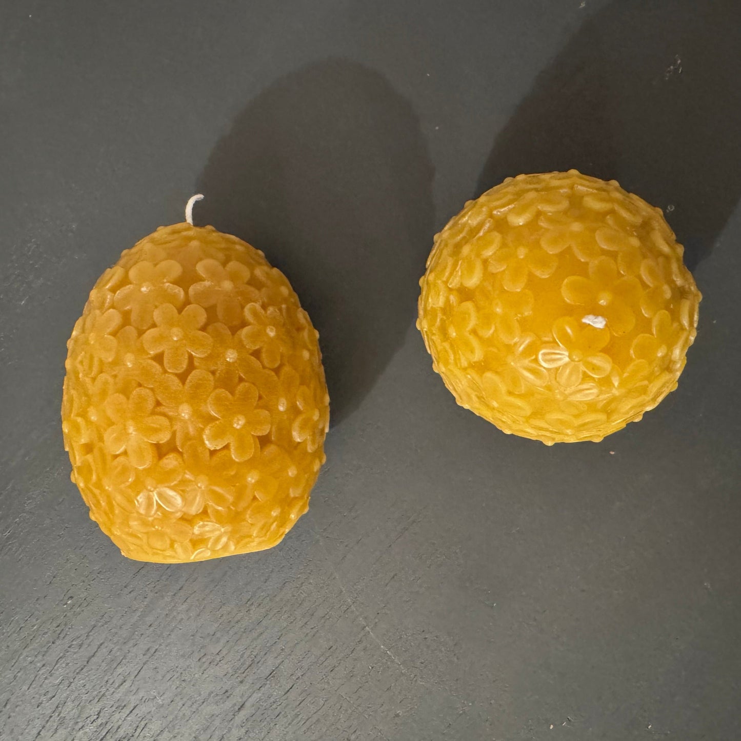 2 egg shaped beeswax candles sit on a grey background, one is on it's side, and one is stood upright. The photo demonstrates both the birds eye view, and the side profile view of these candles