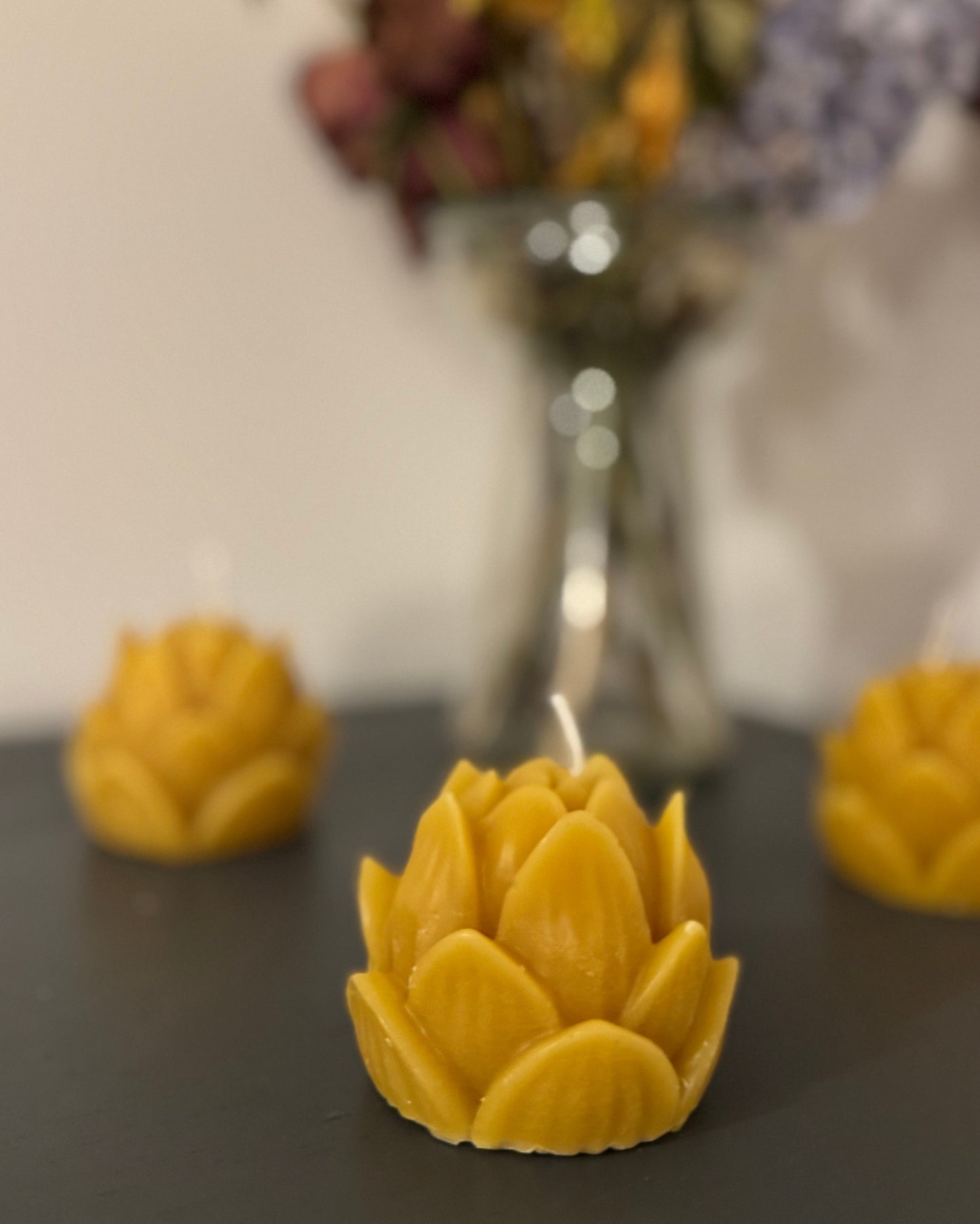 A trio of beeswax candle, positioned in the centre of the screen, with a vase of dried flowers behind, creating a warm, cosy, natural vibe