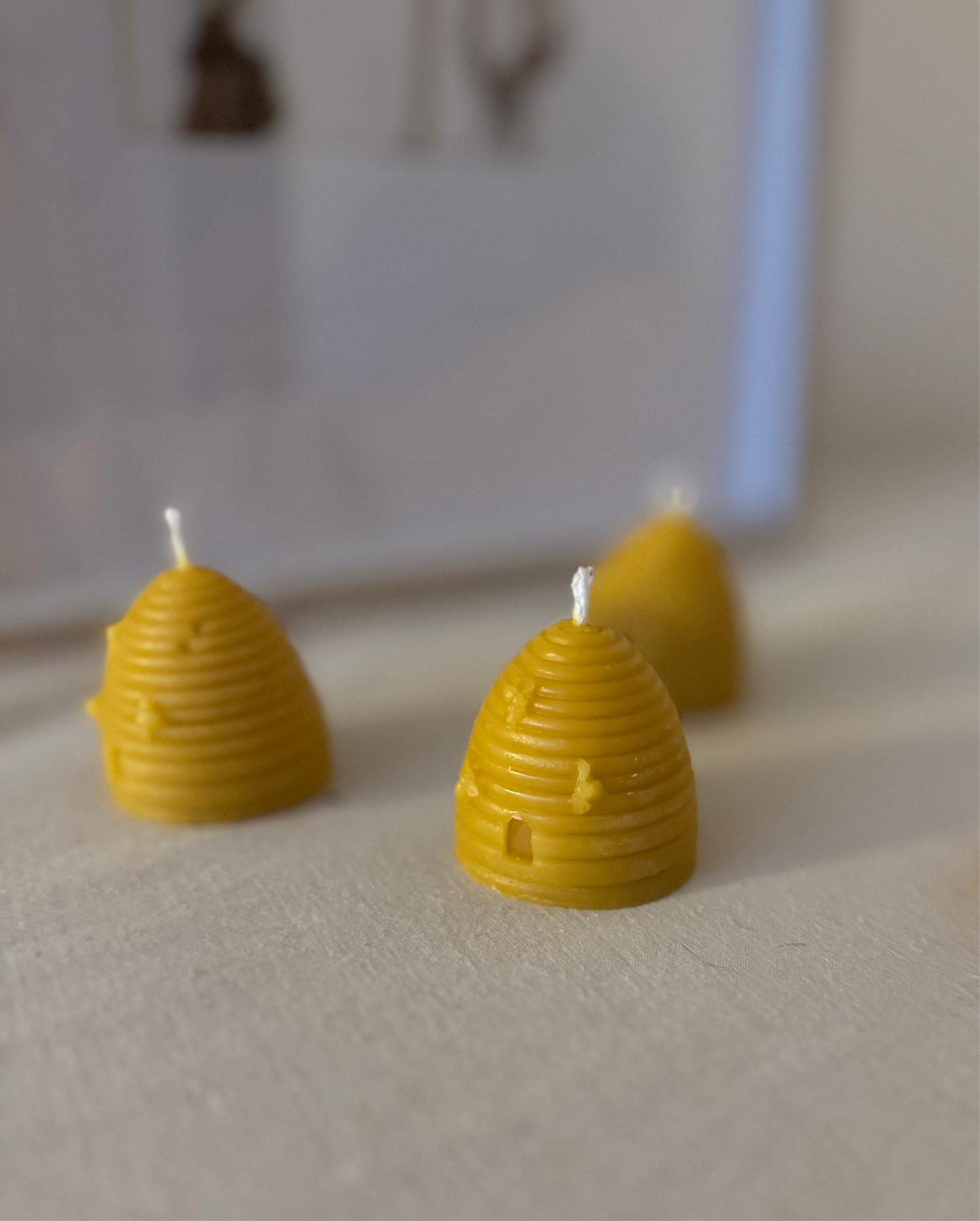 Three handcrafted beehive-shaped beeswax candles displayed on a soft fabric surface, showcasing their natural golden hue and charming design. Perfect eco-friendly home decor with a warm, natural honey aroma and sustainable appeal.
