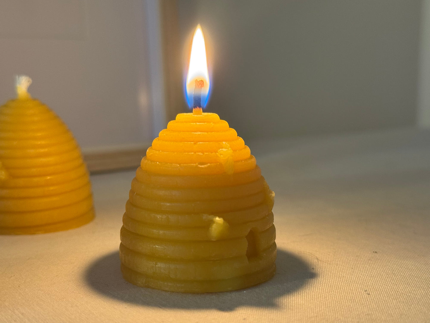 A handcrafted beehive-shaped beeswax candle displayed on a soft fabric surface, showcasing the natural golden hue and charming design. Perfect eco-friendly home decor with a warm, natural honey aroma and sustainable appeal.