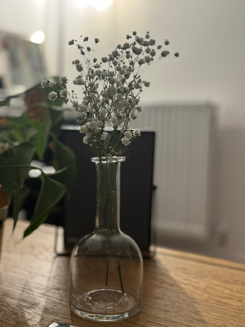 Clear glass vase with small white flowers on a wooden surface