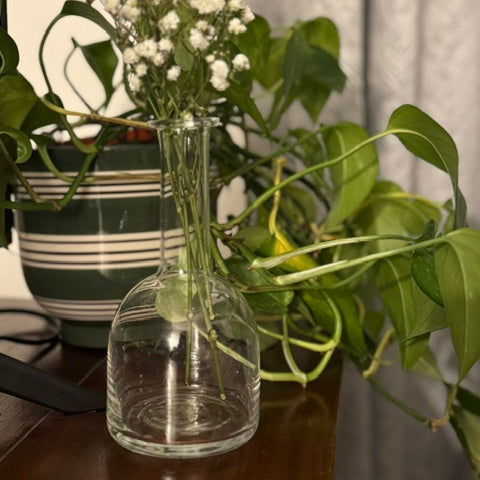 Clear glass vase with greenery and small white flowers on a wooden surface.