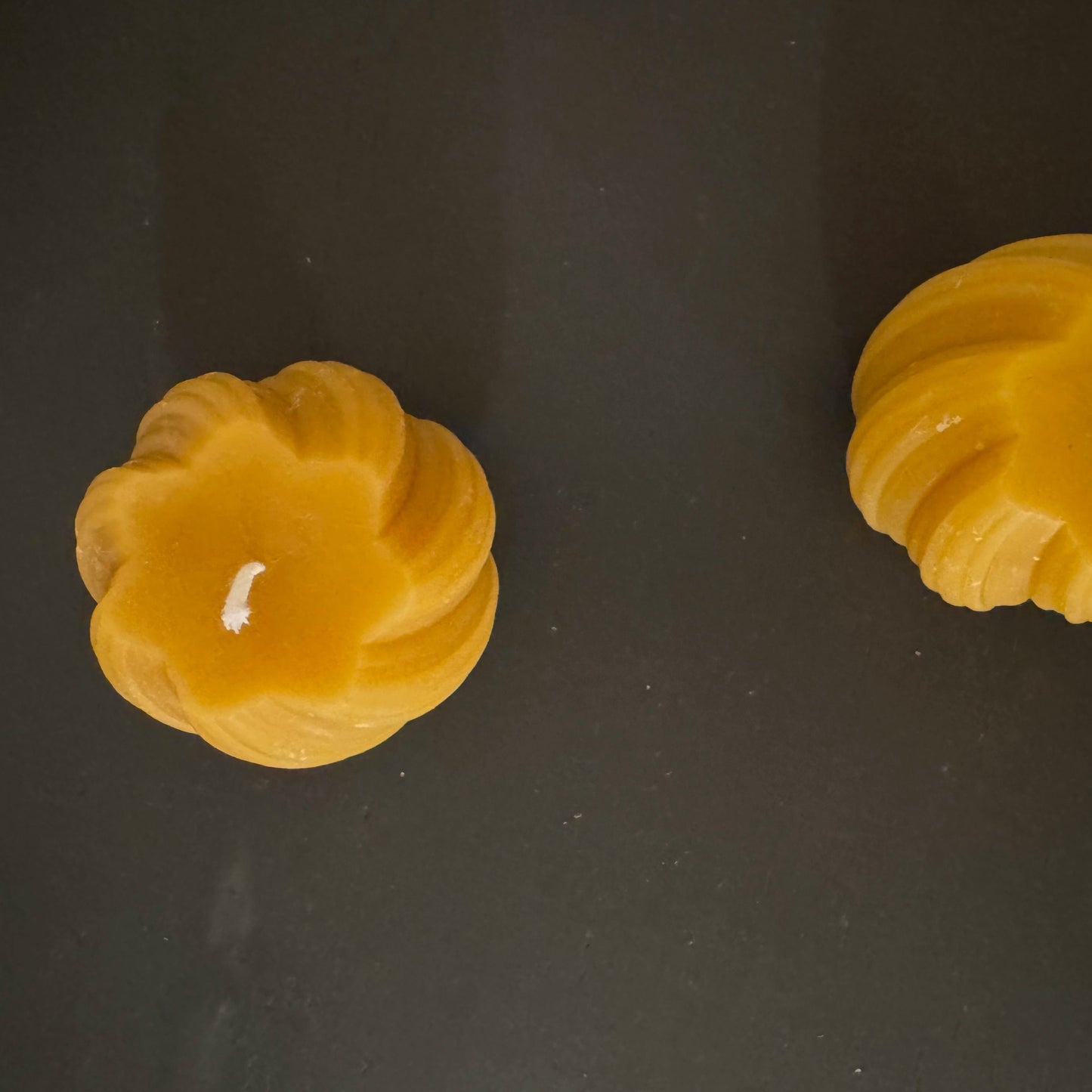 2 beeswax swirled candles sit on a grey sideboard, photographed from above. The photograph is familiar and warm