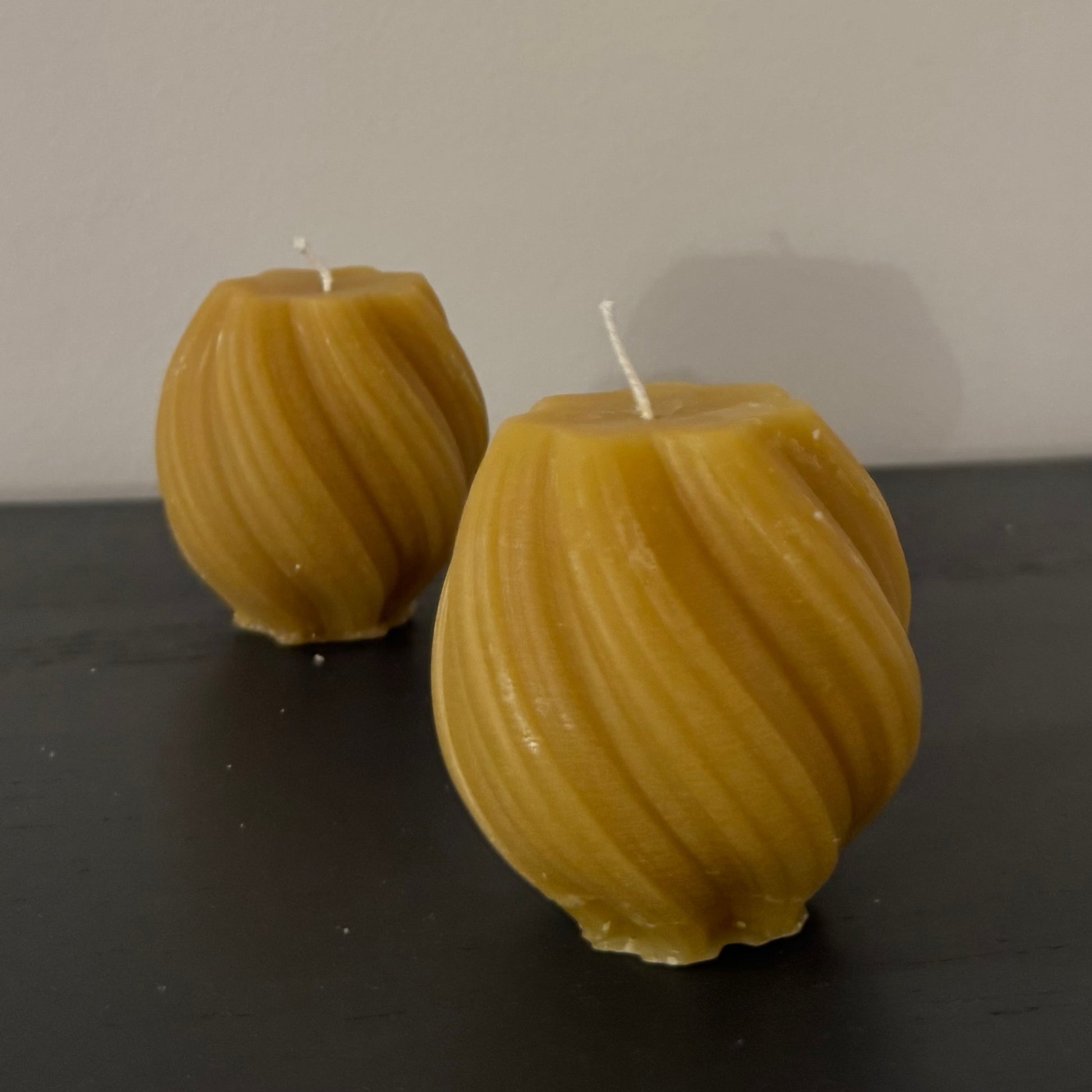 2 beeswax swirled candles sit on a grey sideboard. The photograph is familiar and warm