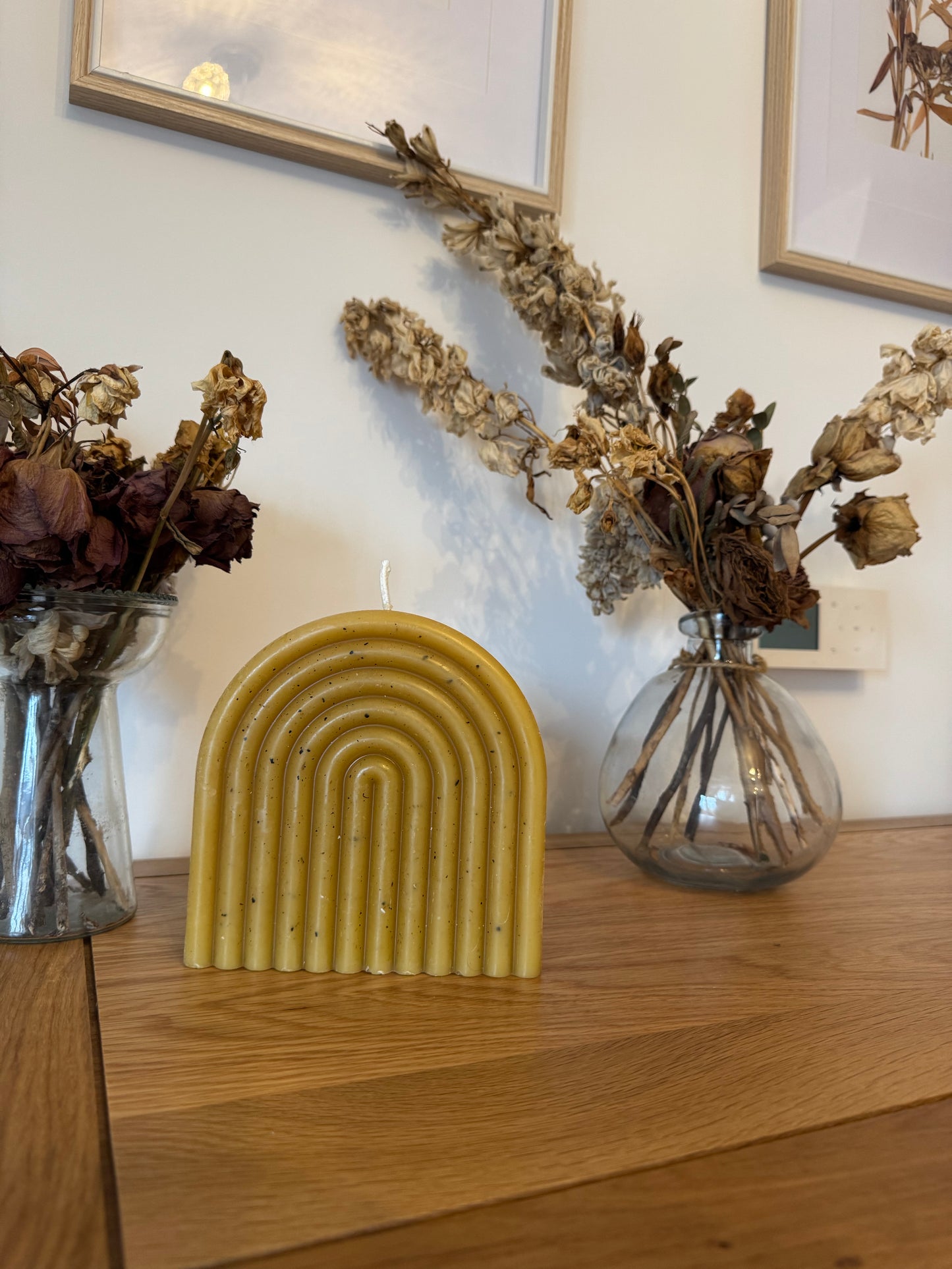 Decorative elements including a freckled beeswax candle arch, dried flowers, and framed pictures on a wall.