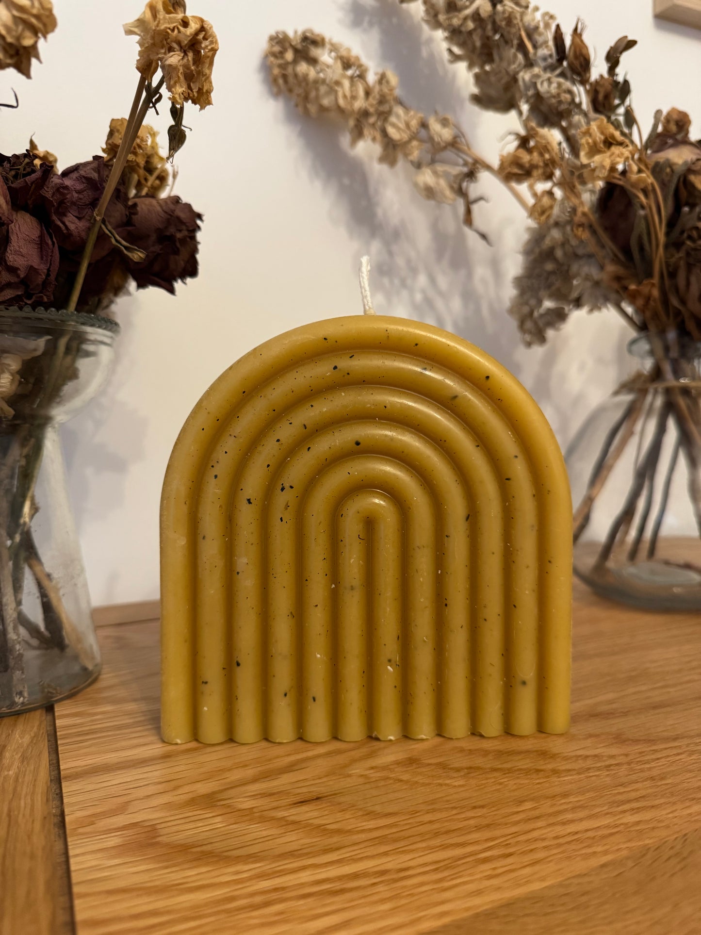Yellow rainbow beeswax candle freckled bar with wavy design on a wooden surface with dried plants