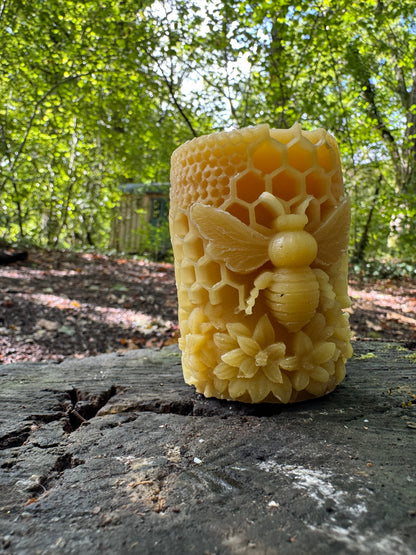 A honeycomb moulded beeswax candle with ornate bee detailing sits in a woodland environment reminiscent of its natural appeal 