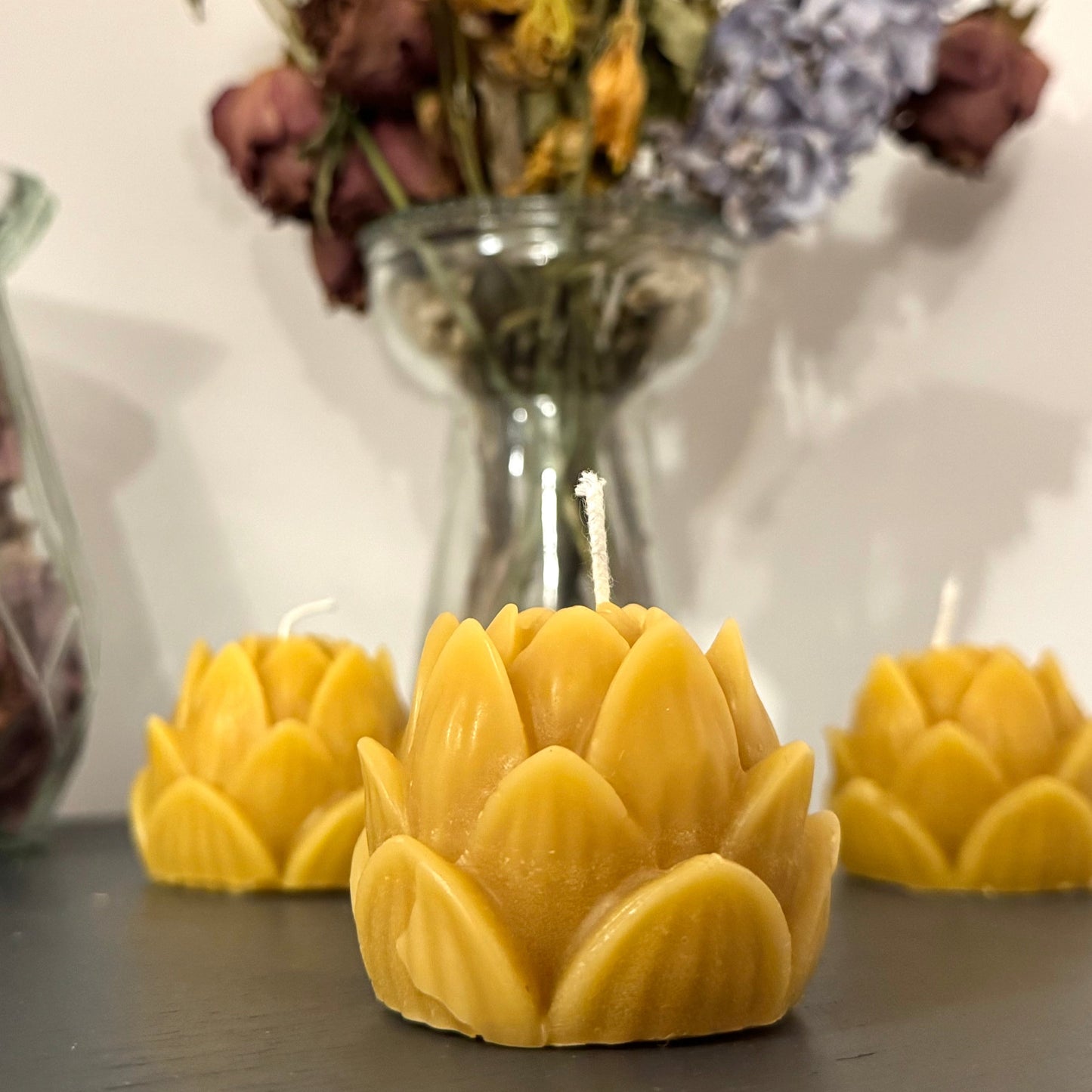 A trio of beeswax candle,  positioned in the centre of the screen, with a vase of dried flowers behind, creating a warm, cosy, natural vibe