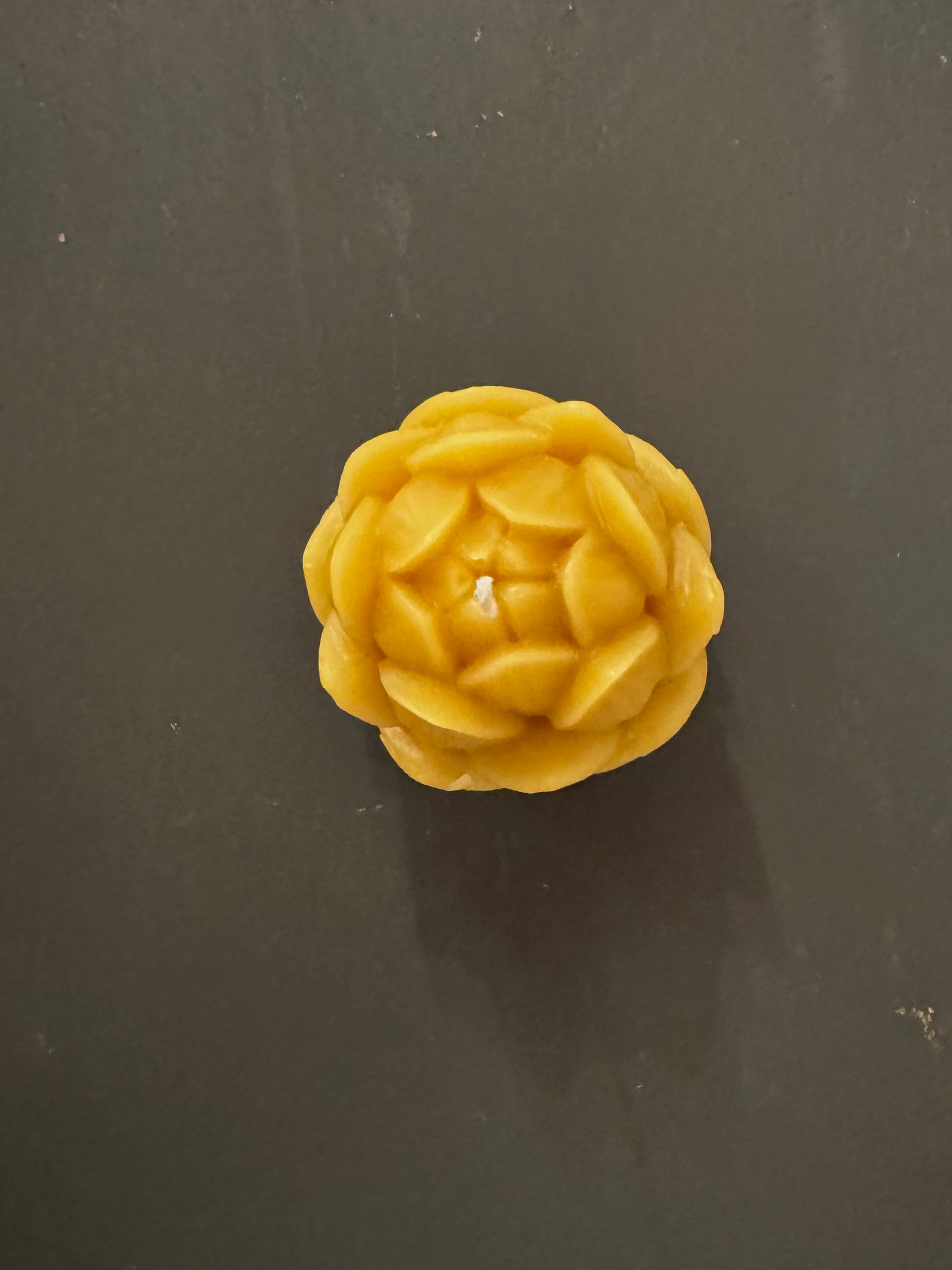 A birds eye view of a singular beeswax candle,  positioned in the centre of the screen, with a warm, cosy, natural vibe