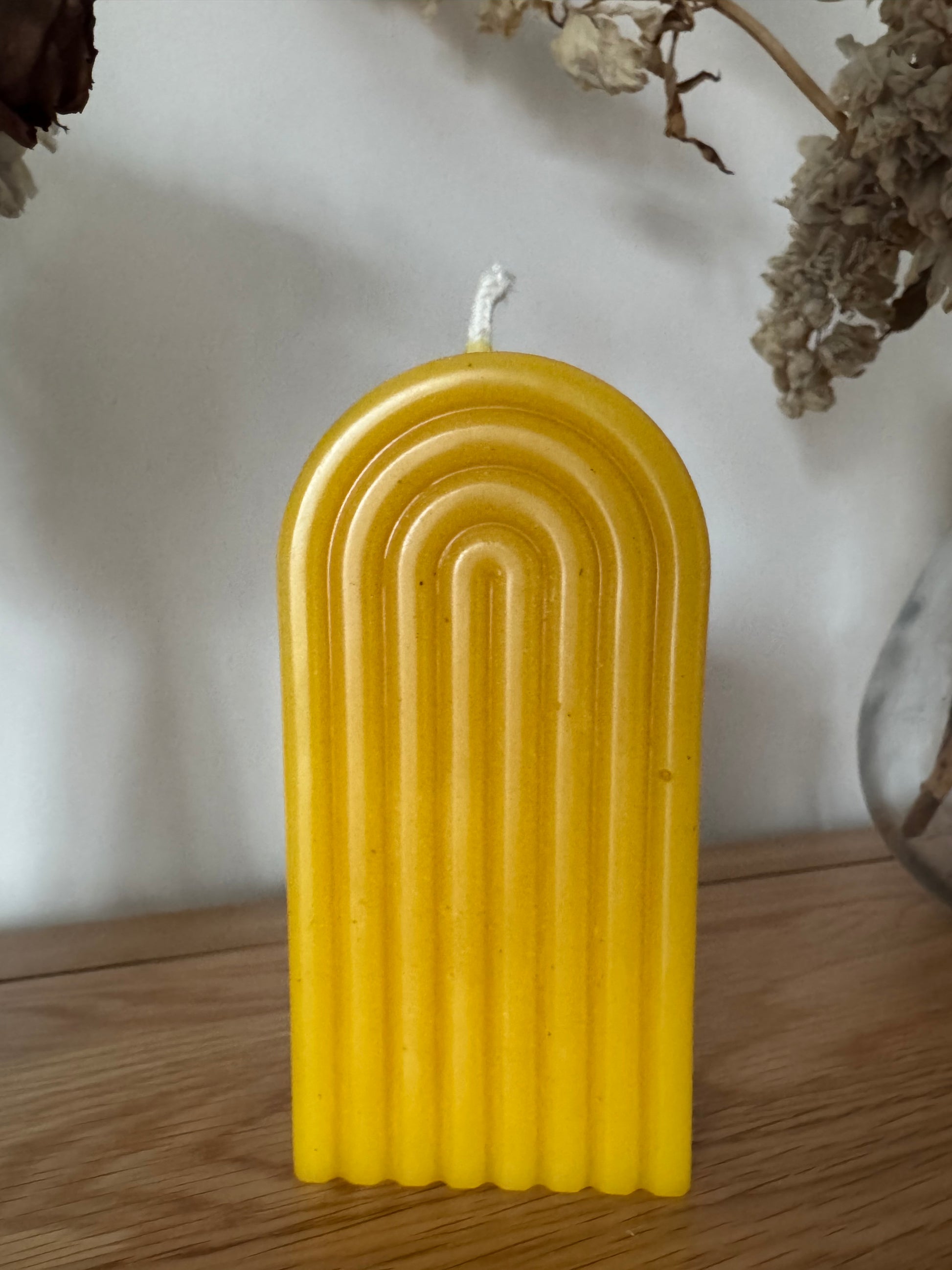 Yellow arch beeswax candle on a white surface with a wooden side panel.