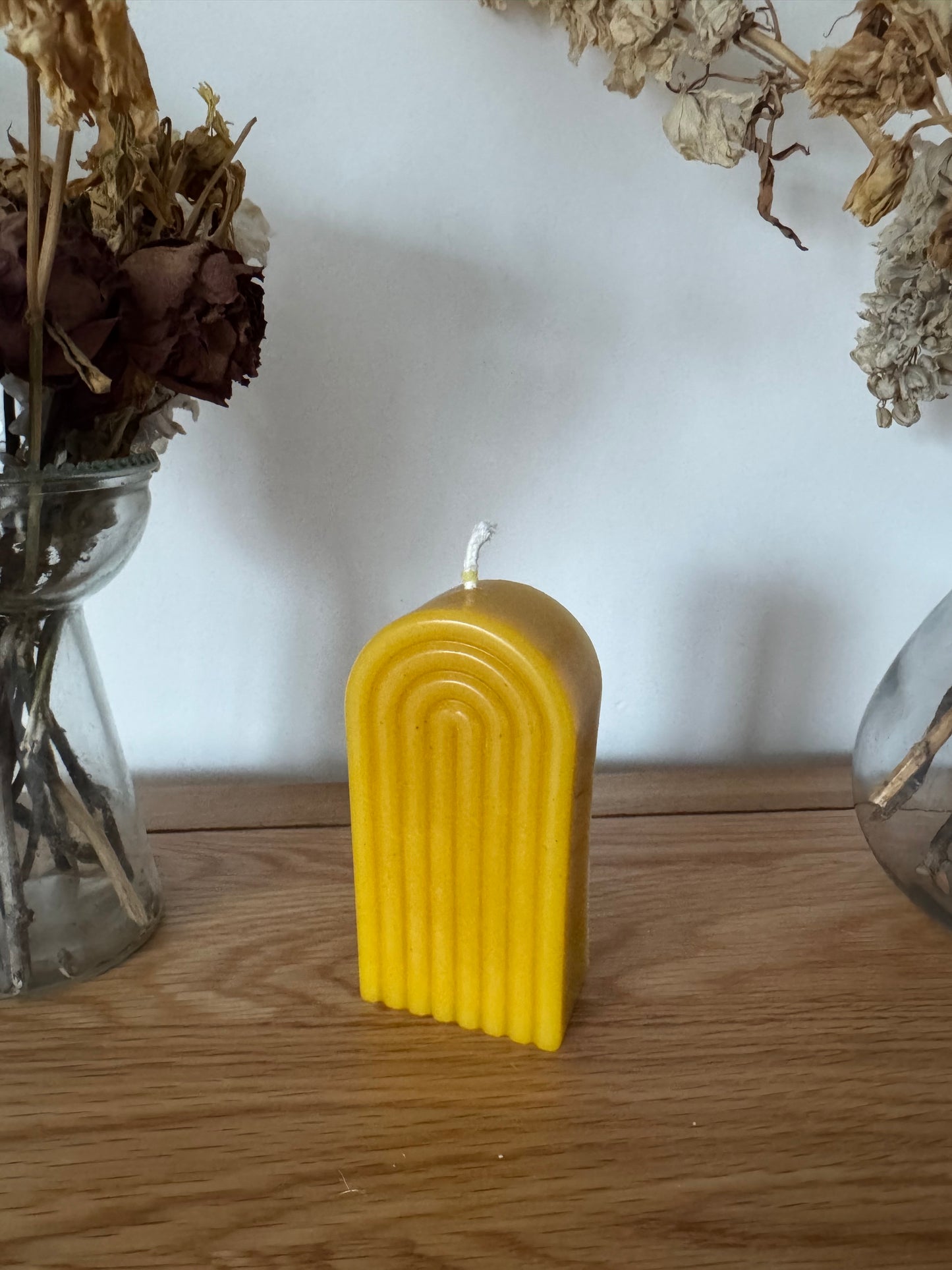 Beeswax arch column on a wooden surface with dried plants in the background