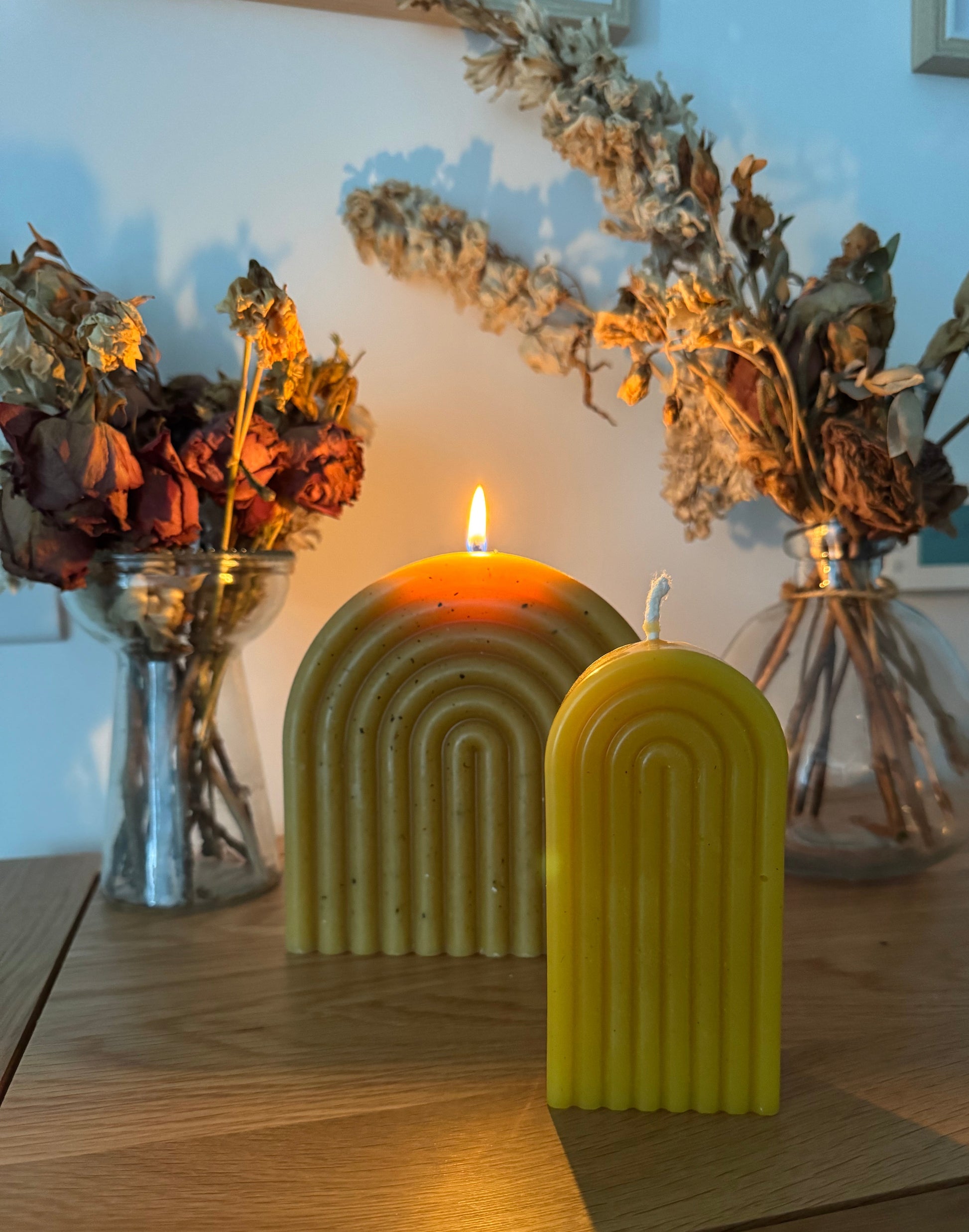 Yellow beeswax candles on a wooden surface with decorative dried flowers.