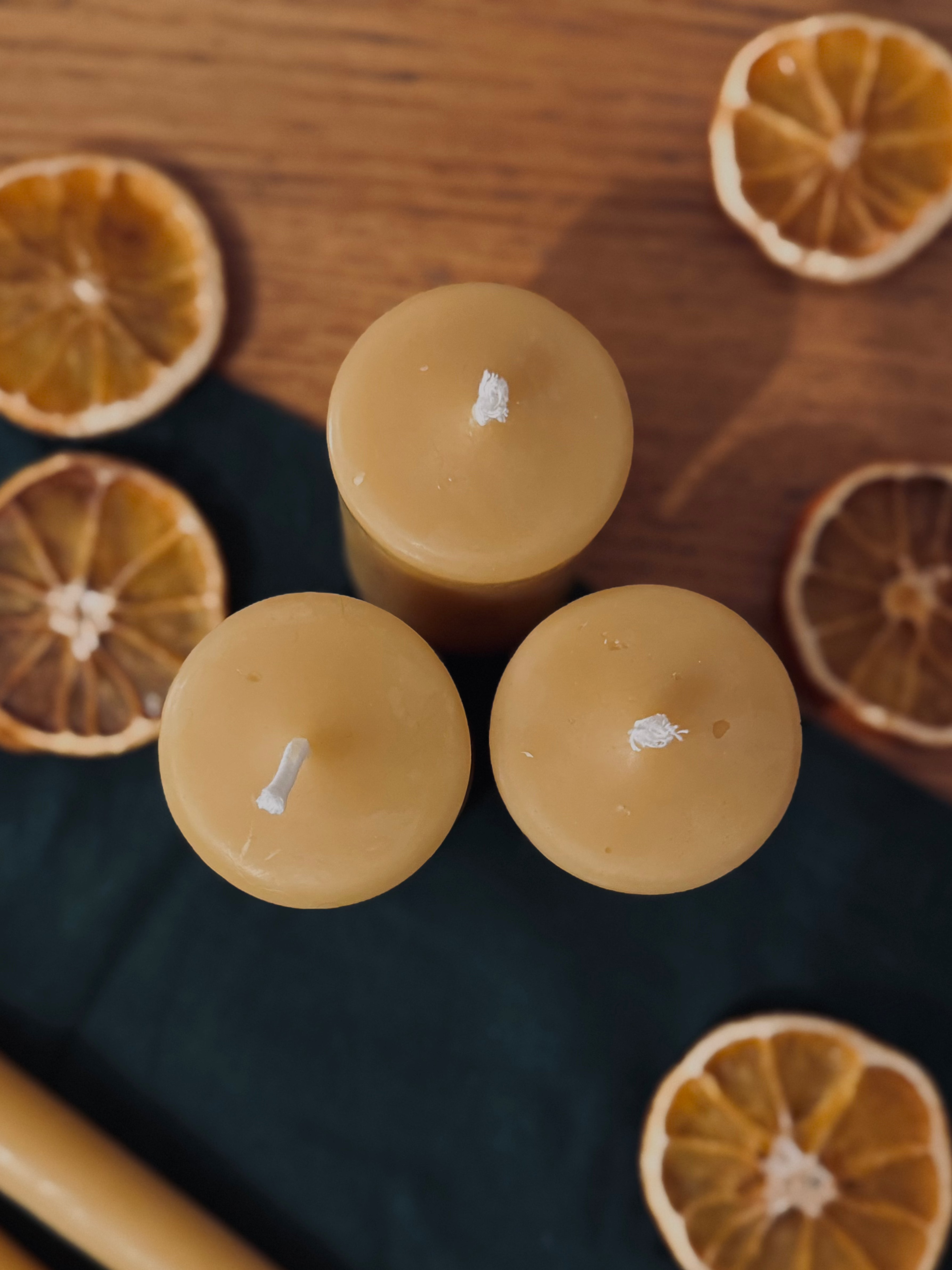 Three beeswax candles in a trio surrounded by natural dehydrated oranges from above. 