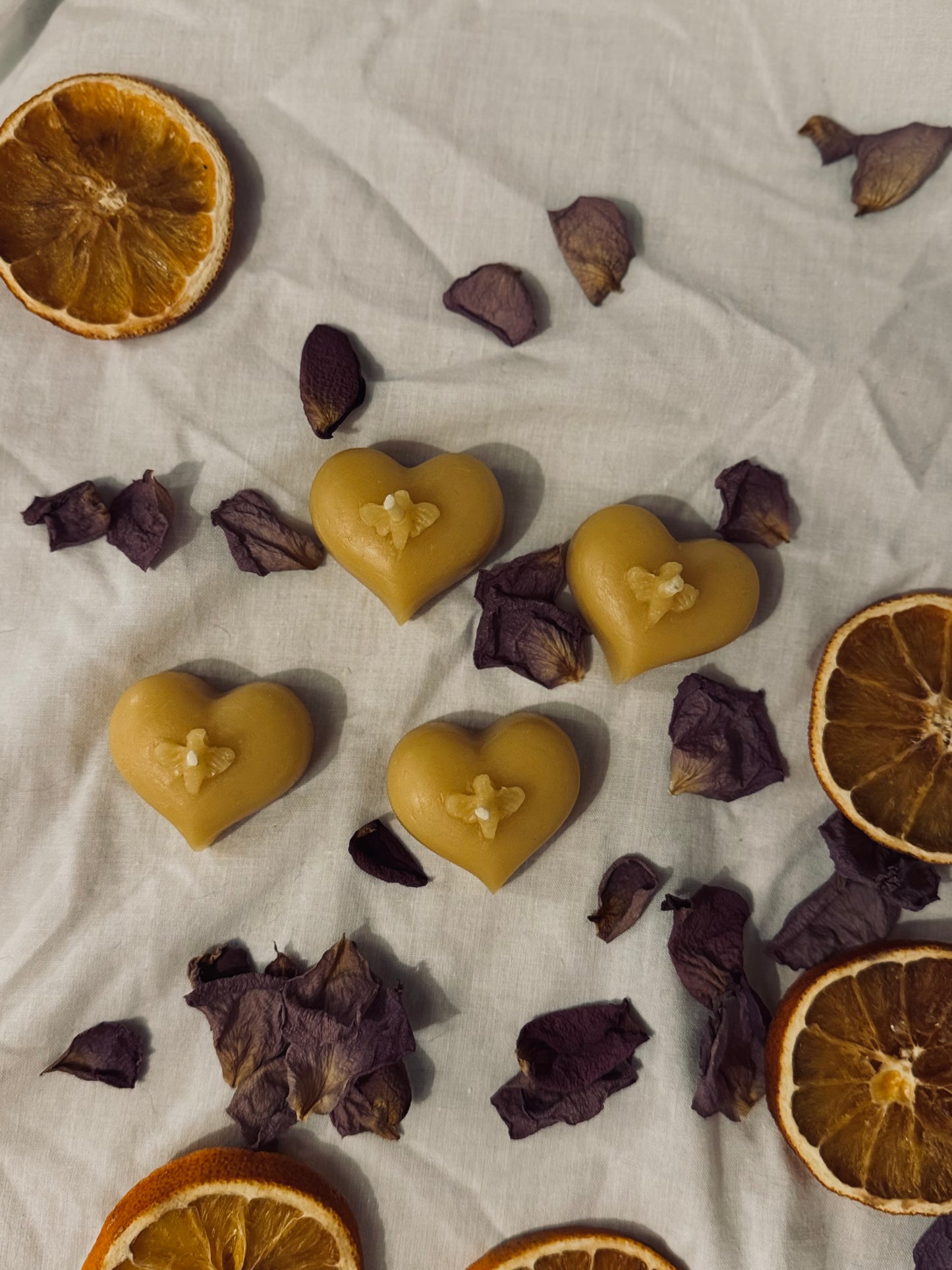 This image features four natural beeswax candles on a white sheet with dried petals around. It's an eco friendly appearance and encourages use of natural products