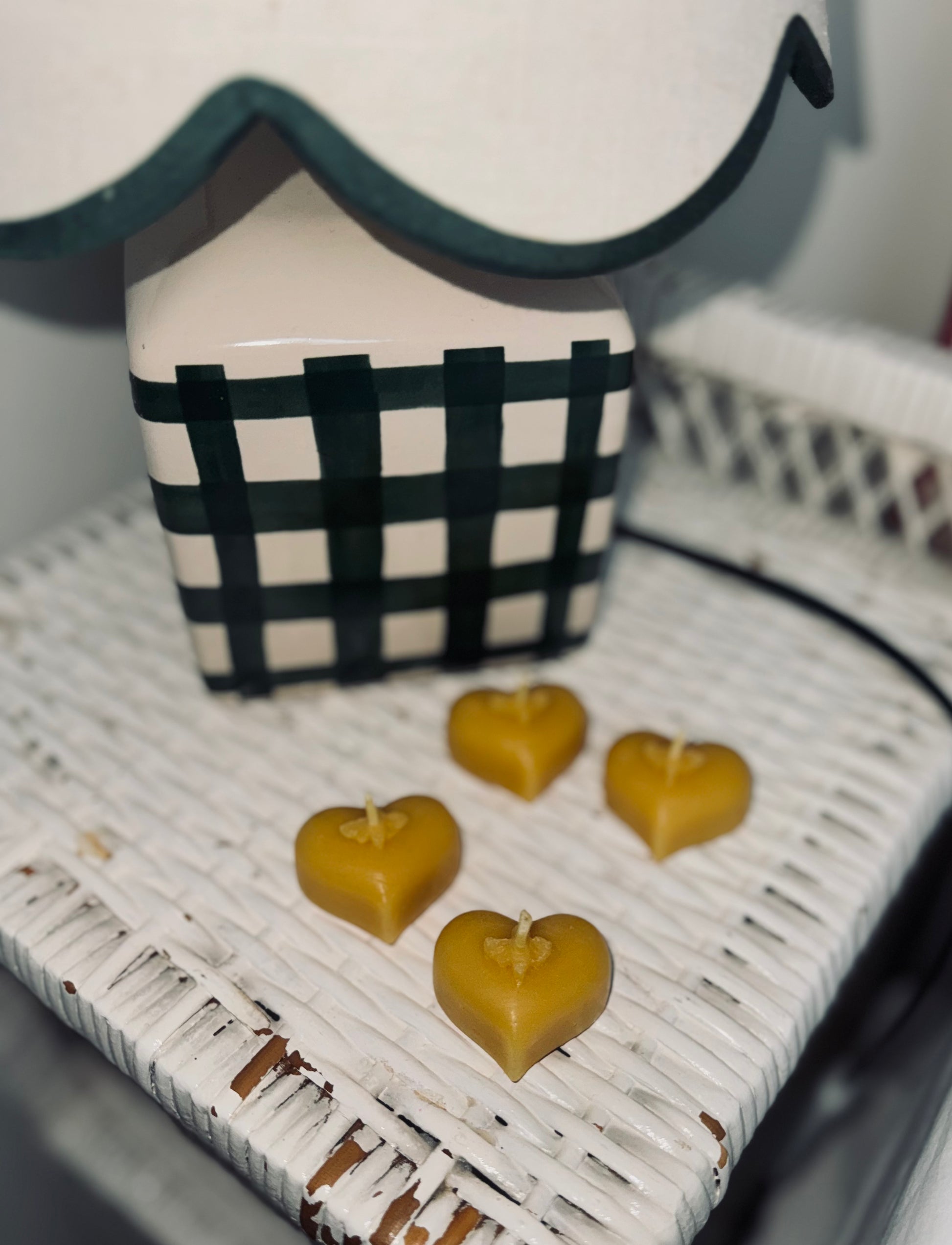 The image consists of four natural beeswax tealights set against a white wicker stand, with cosy gingham lamp with scalloped edges. It has a warm and inviting feel 