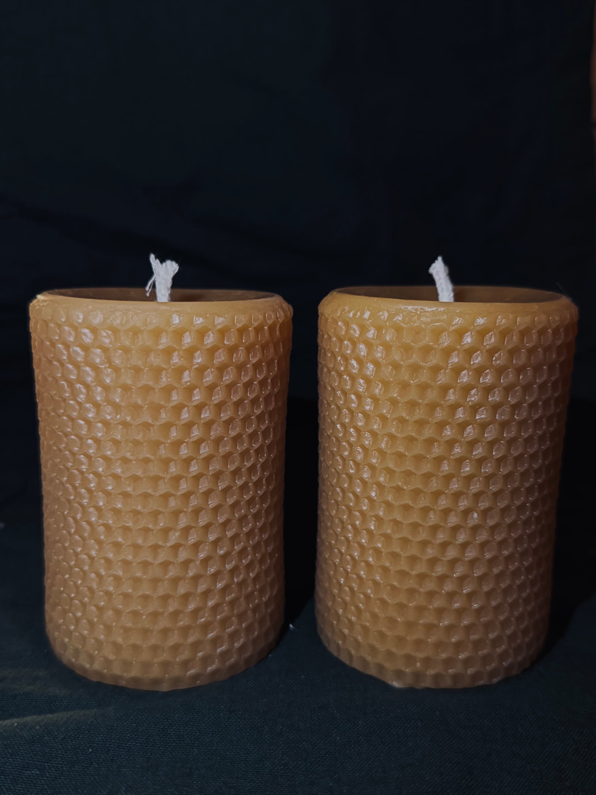 This image features a pair of honeycomb imprinted beeswax candles which stands alone against a dark backdrop with dehydrated oranges surrounding the base. It shows a studio style lighting, allowing you to appreciate the honeycomb printing on the beeswax candles