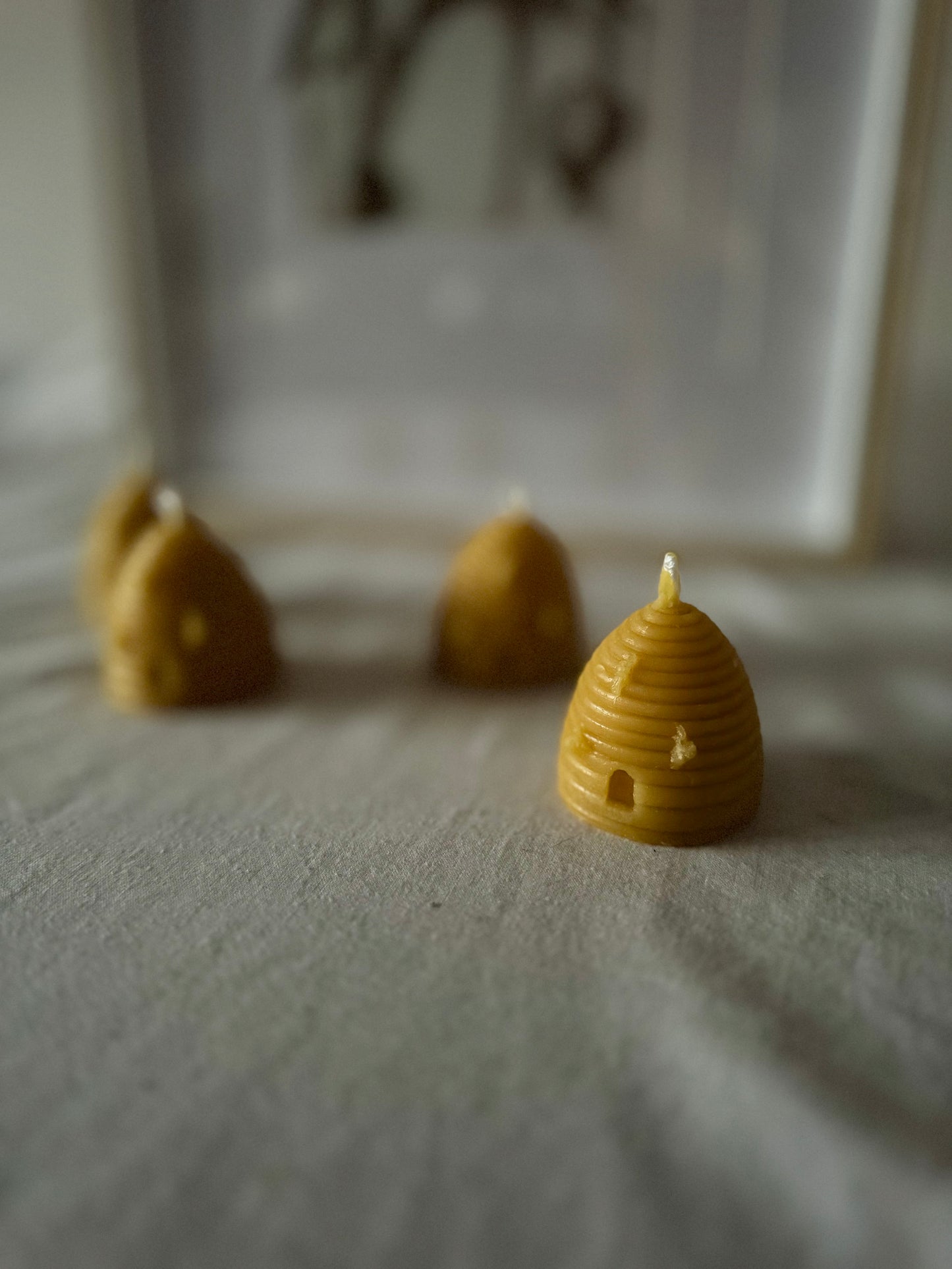 Four handcrafted beehive-shaped beeswax candles displayed on a soft fabric surface, showcasing their natural golden hue and charming design. Perfect eco-friendly home decor with a warm, natural honey aroma and sustainable appeal.