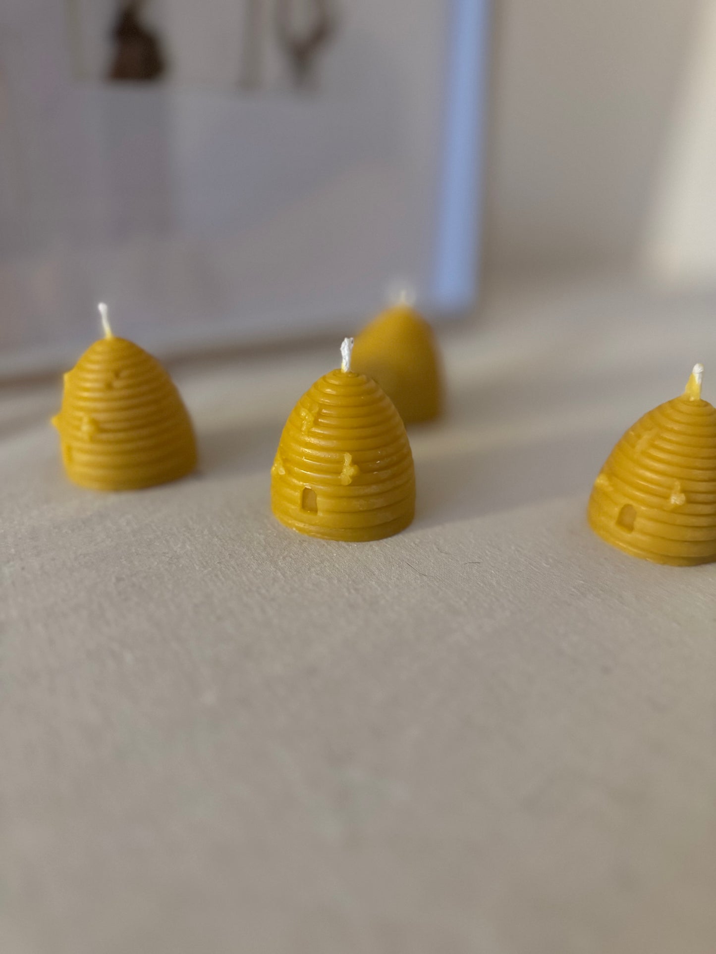 Four handcrafted beehive-shaped beeswax candles displayed on a soft fabric surface, showcasing their natural golden hue and charming design. Perfect eco-friendly home decor with a warm, natural honey aroma and sustainable appeal.