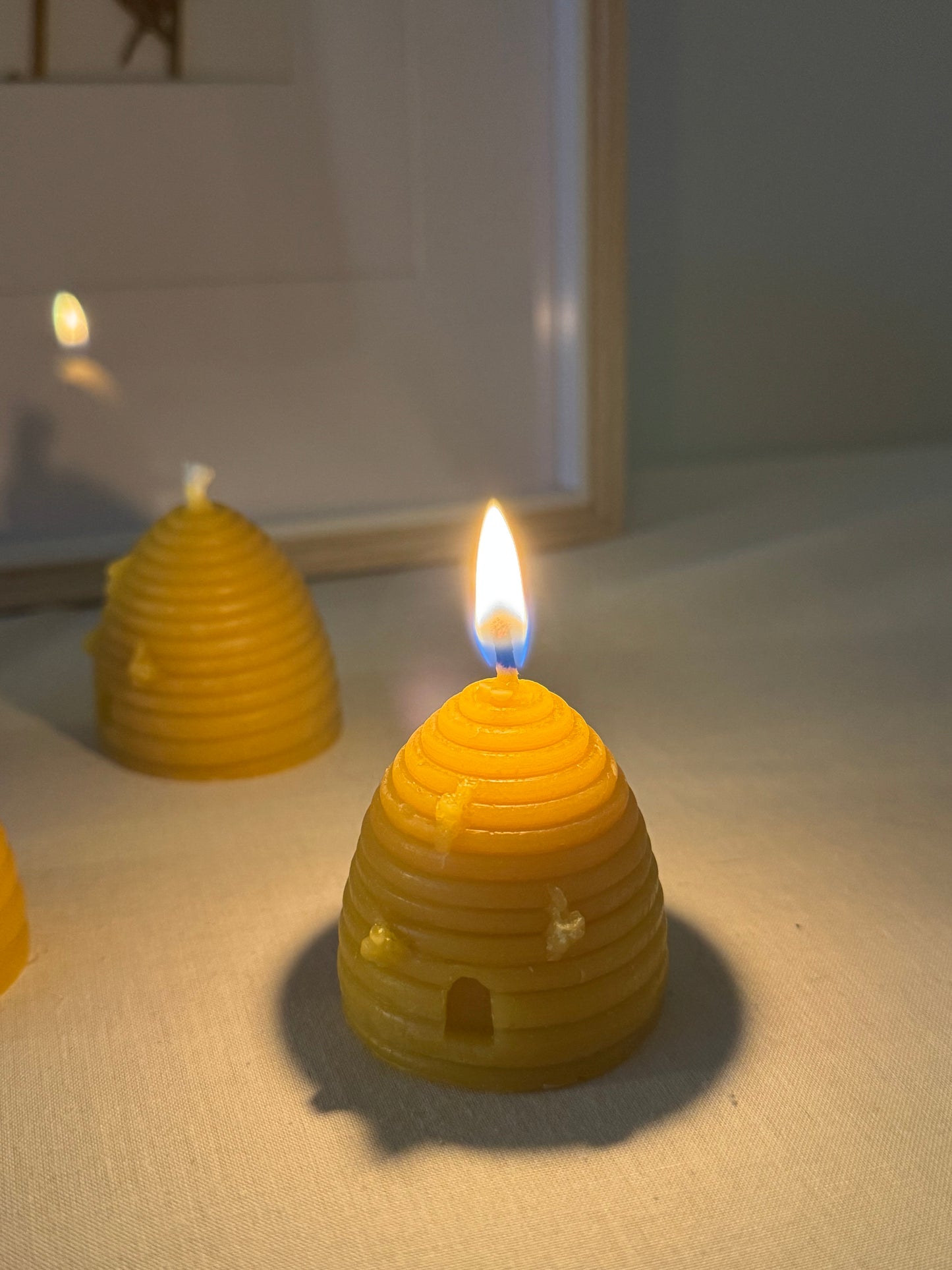 Two handcrafted beehive-shaped beeswax candles displayed on a soft fabric surface, showcasing their natural golden hue and charming design. Perfect eco-friendly home decor with a warm, natural honey aroma and sustainable appeal.