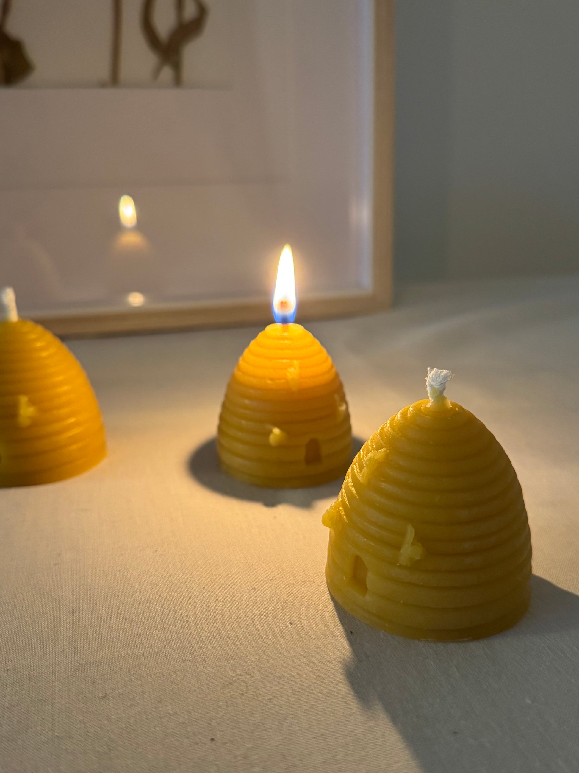 Three handcrafted beehive-shaped beeswax candles displayed on a soft fabric surface, showcasing their natural golden hue and charming design. Perfect eco-friendly home decor with a warm, natural honey aroma and sustainable appeal.