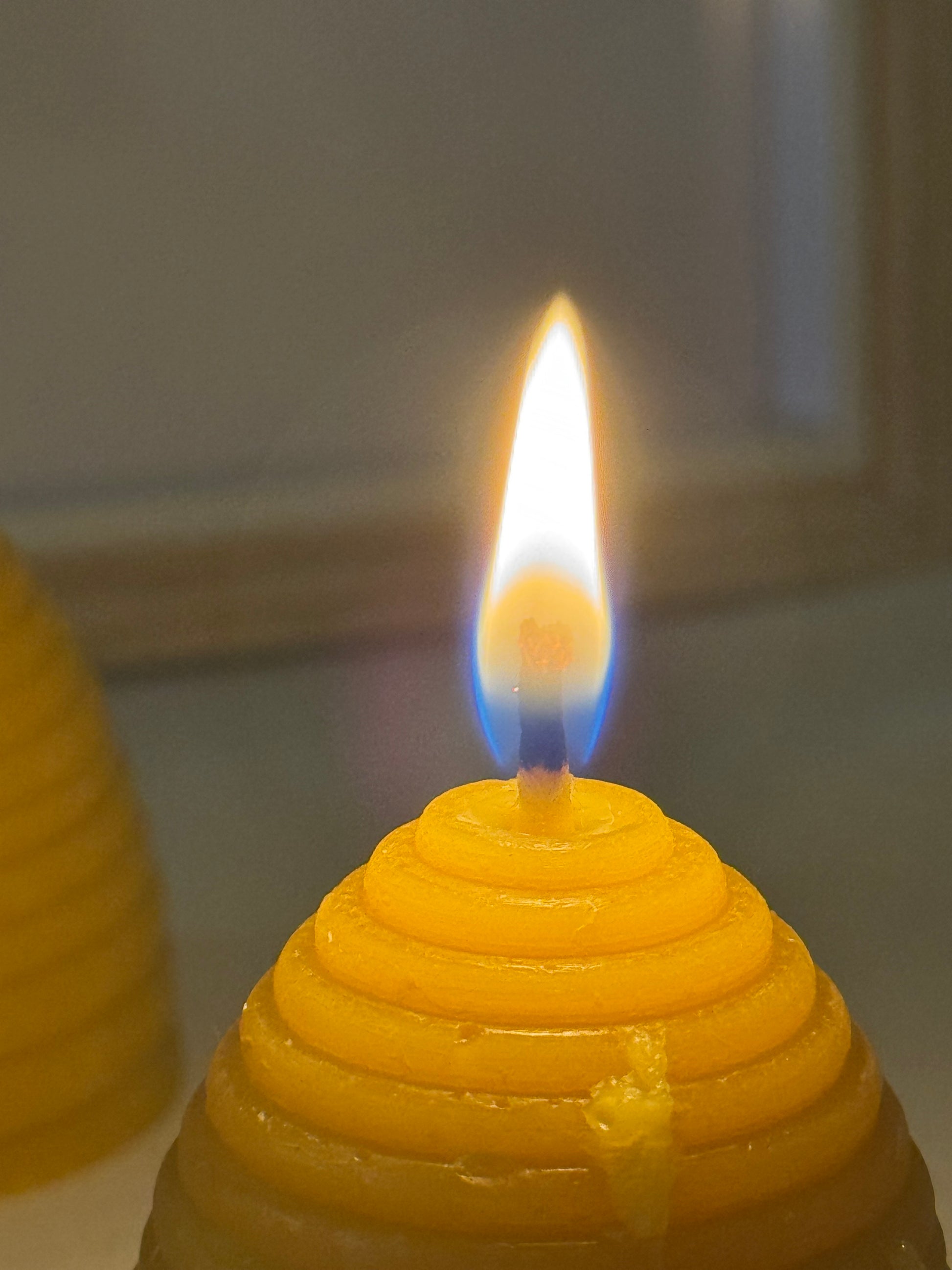 A handcrafted beehive-shaped beeswax candle displayed on a soft fabric surface, showcasing the natural golden hue and charming design. Perfect eco-friendly home decor with a warm, natural honey aroma and sustainable appeal. The flame is pure and golden. 