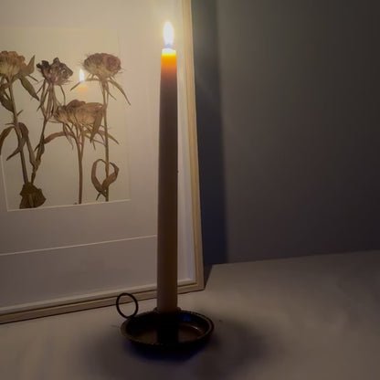 A slow moving video showing the flame of the natural beeswax taper candle against a rustic dried flower backdrop  creating a warm environment