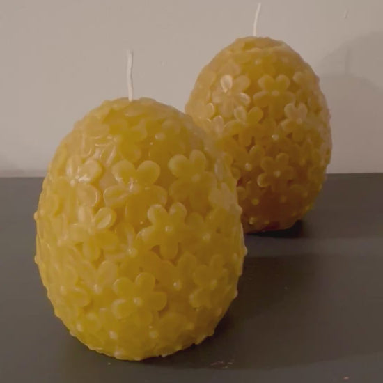 2 egg shaped domed floral candles sit in front of a white background