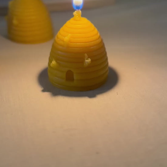A video of a beehive skep shaped beeswax candle burning slowly, then panning to show another three beehive skep shaped beeswax candles behind. They emit a soft glow, creating a cosy and relaxed atmosphere, showcasing natural products and sustainable living. 