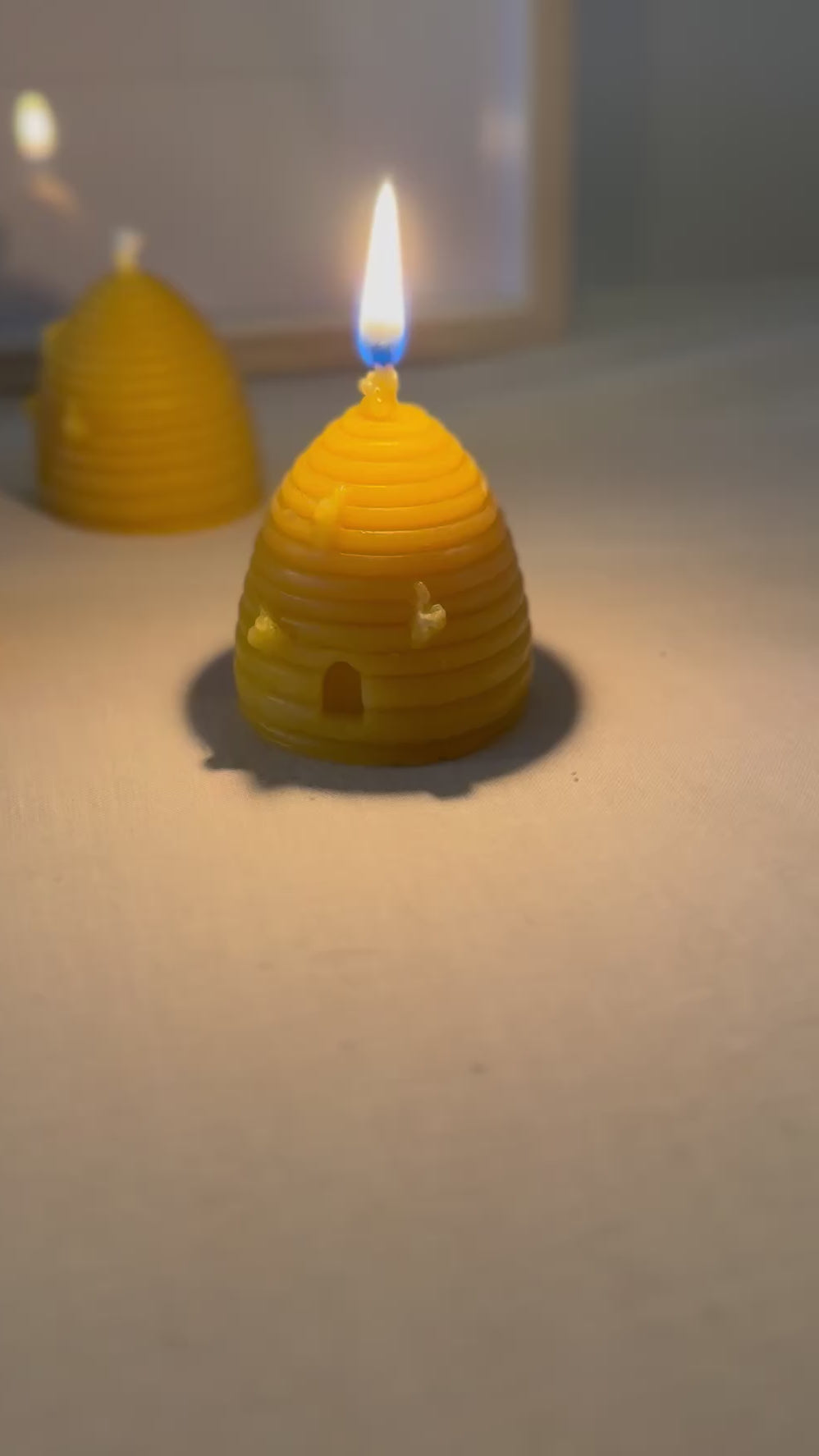 A video of a beehive skep shaped beeswax candle burning slowly, then panning to show another three beehive skep shaped beeswax candles behind. They emit a soft glow, creating a cosy and relaxed atmosphere, showcasing natural products and sustainable living. 